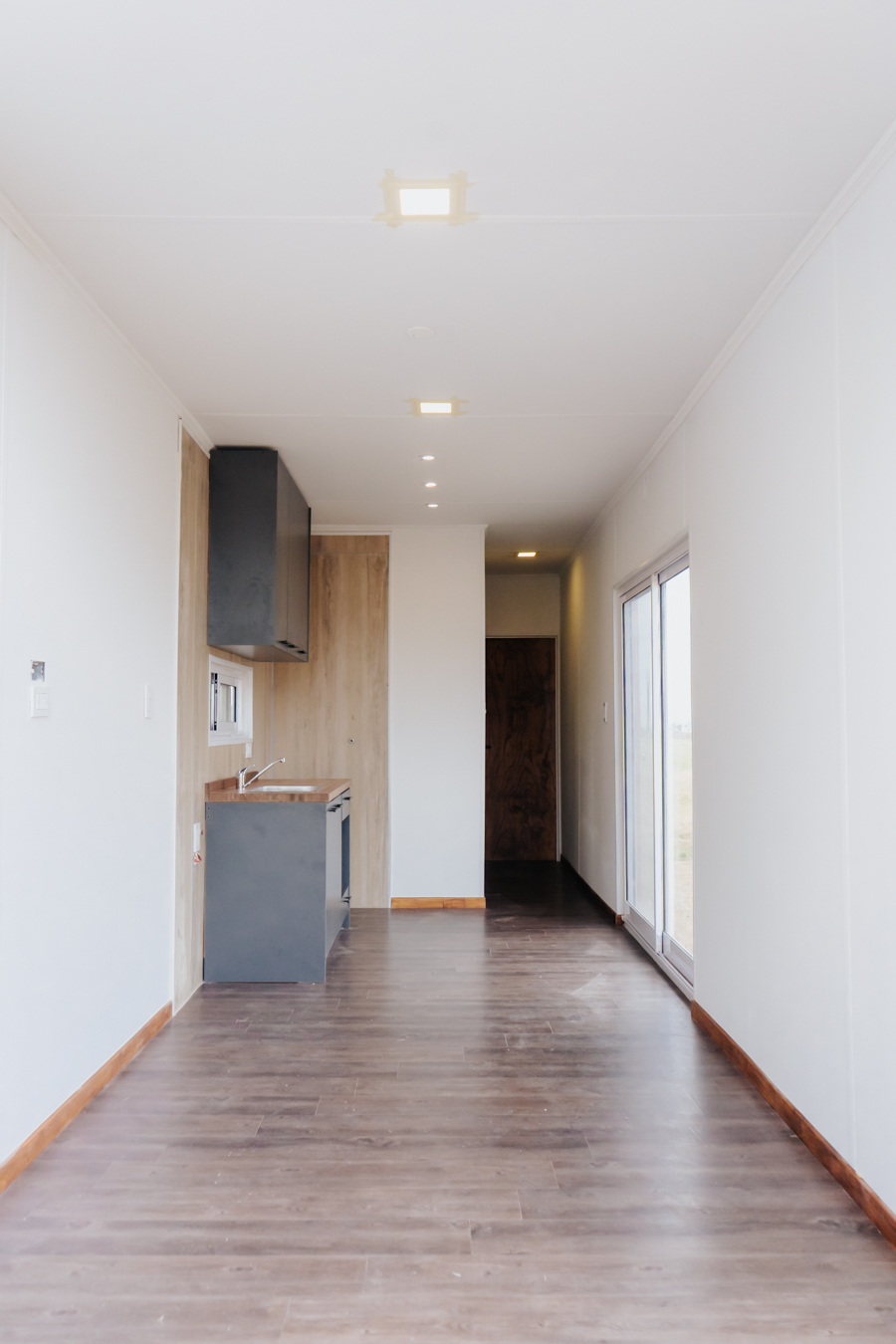 Interior luminoso del módulo con piso símil madera y cocina al fondo
