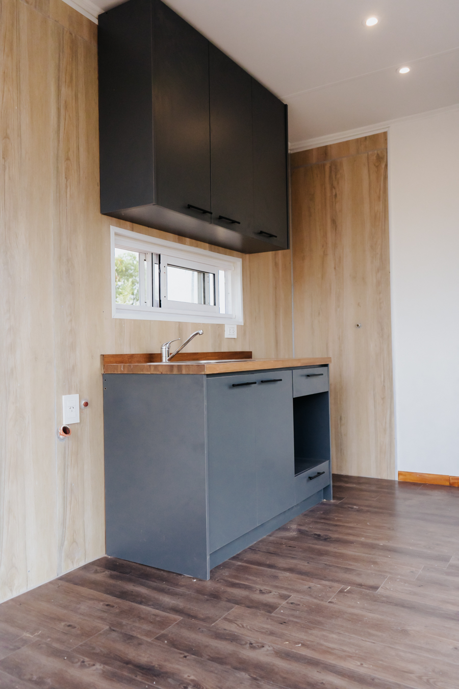 Cocina compacta con mobiliario oscuro y revestimiento símil madera