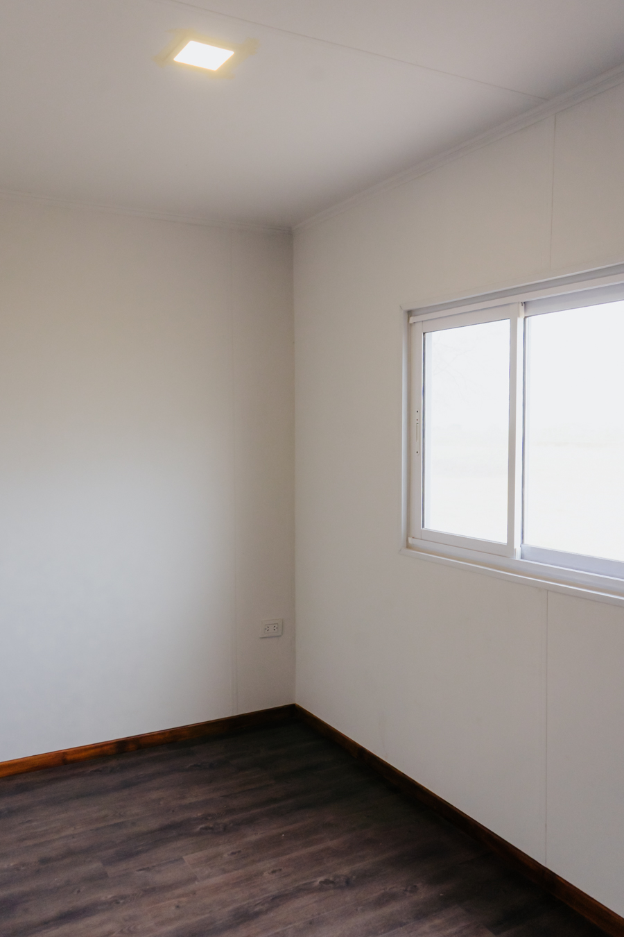 Dormitorio con piso oscuro, pared blanca y ventana